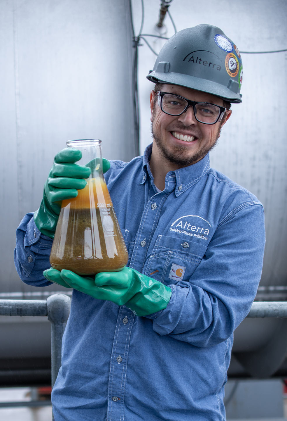 Man wearing a hard hat holding a beaker of oil